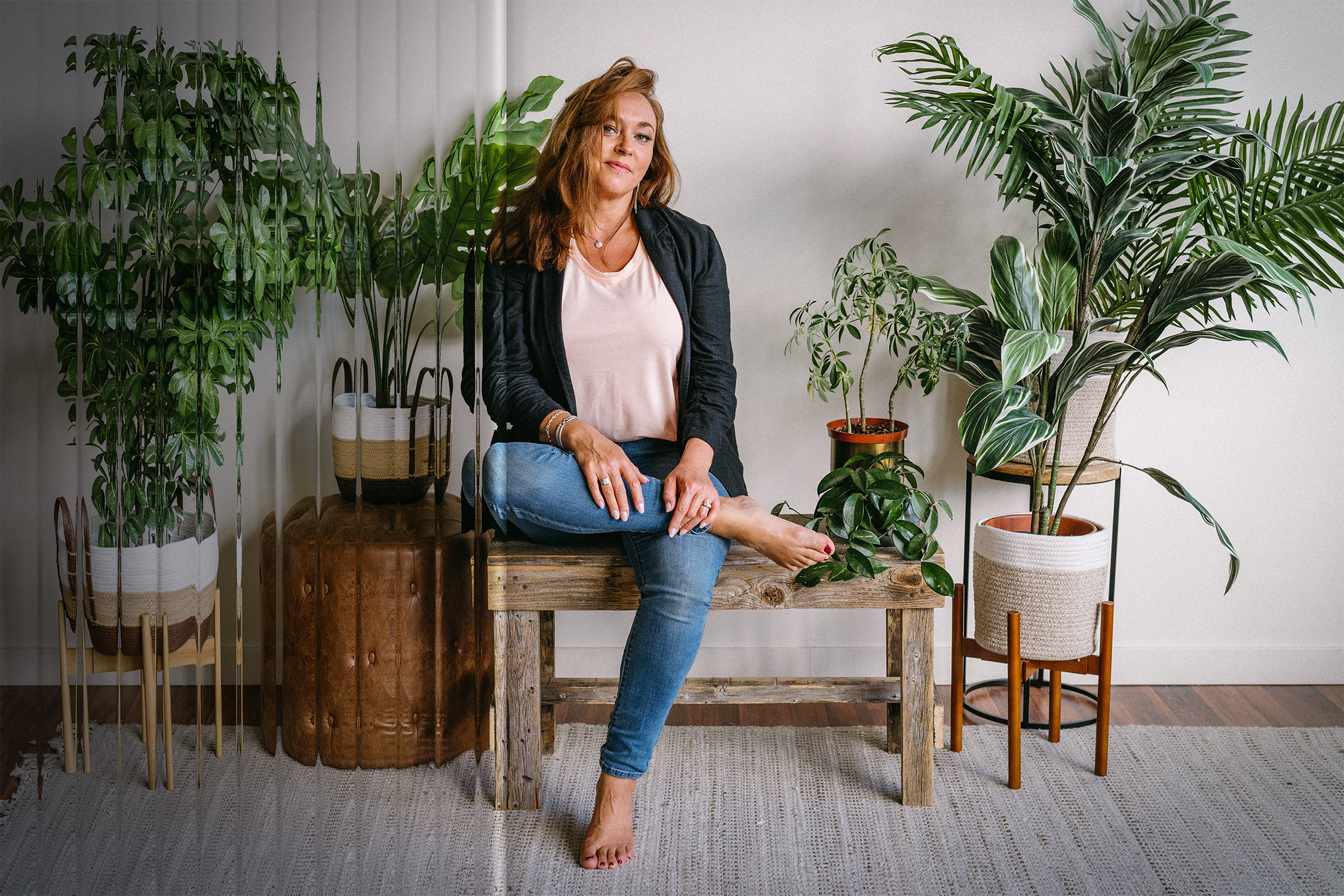Elizabeth Miner sits on a rustic wooden bench in a casual studio space with potted plants. A clear reeded glass texture overlays part of the image.
